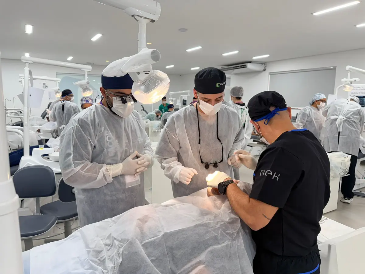 A hall of dental units at the Brazil campus: several teams in gowns and masks operating on draped patients at the same time, under the surgical lights